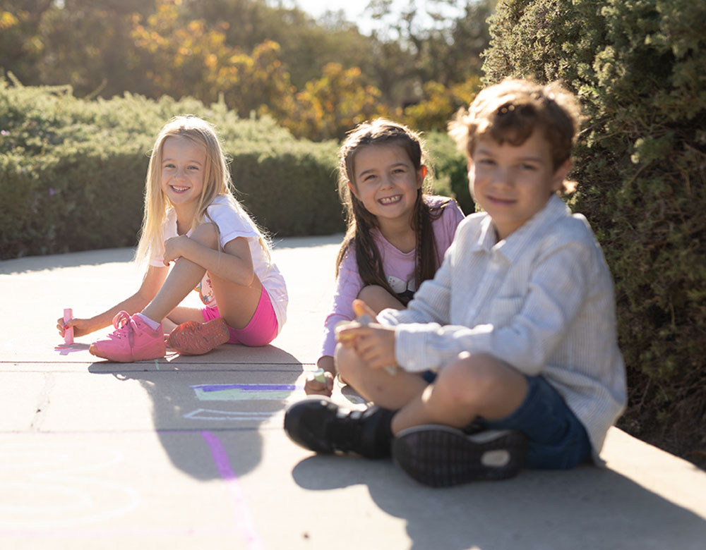 Three young children drawing on the pavement in a community focuses, family friendly land development in Perth